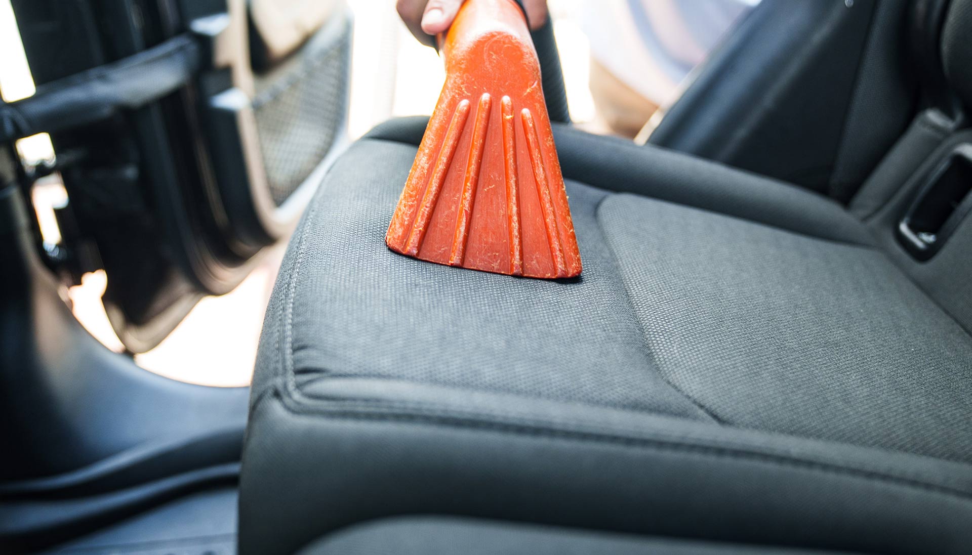 An interior view of a vacuum station, featuring a person using the vacuum to clean the car’s interior, with the vacuum hose and attachments clearly visible in action.